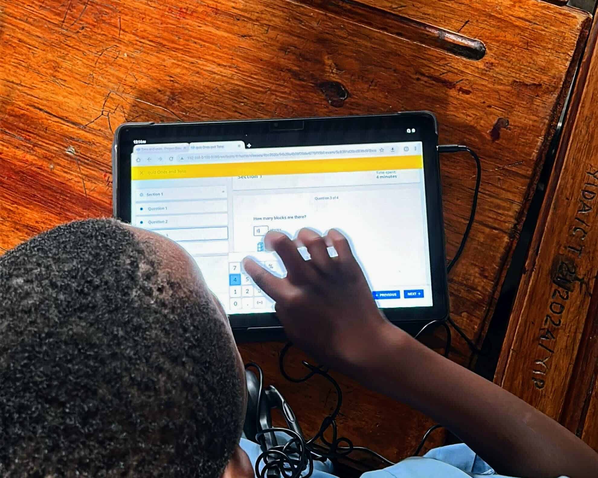 Student using a tablet to complete an interactive math quiz at a wooden desk