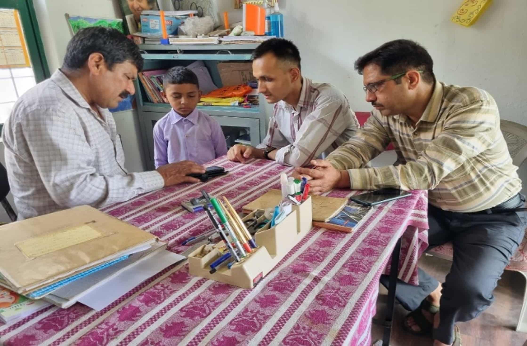 Group of teachers and a parent discussing a student’s progress around a table in a classroom setting with school supplies