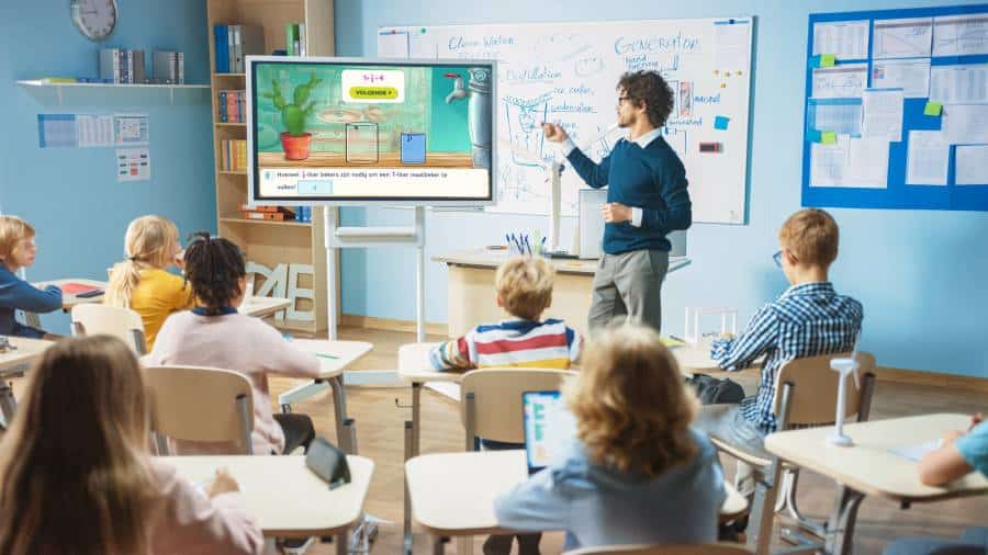 Teacher using an interactive whiteboard to teach a classroom of elementary students with digital devices