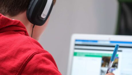Student wearing headphones and using a laptop while holding a pen, focused on digital learning