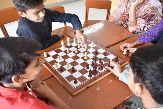 Children playing a game of chess together at a school desk.