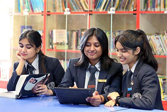 Students studying and collaborating in a library setting Three students in school uniforms are sitting at a table in a library, engaging with books and a tablet