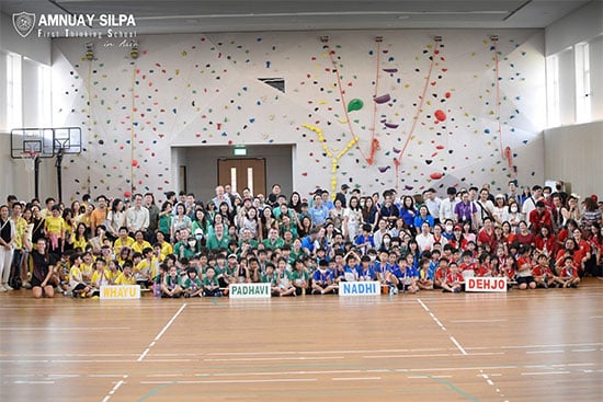 Students gather for inter-house sports event at school gymnasium Large group photo of students and teachers in different house colors during a school sports event in the gymnasium.