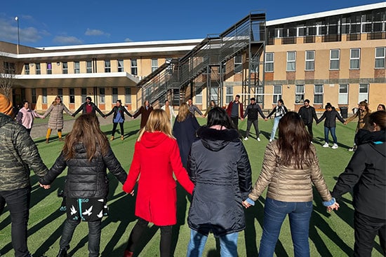 People participating in a group activity outside a building Group of people holding hands in a circle outdoors with a building in the background