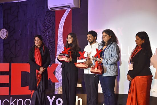 A group of people standing on stage at a TEDx event holding awards. They are posing with a TEDx backdrop in the background