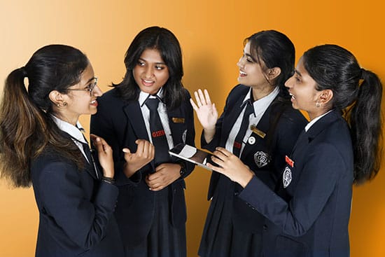 Group of students discussing something on a tablet Four students in school uniforms interacting and smiling while holding a tablet