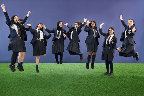 Group of happy students celebrating in school uniforms Group of eight female students in school uniforms jumping with joy on a grassy field with a purple background