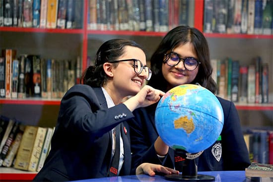 Students exploring the world with a globe in a library Two students in school uniforms are smiling and pointing at a globe in a library setting