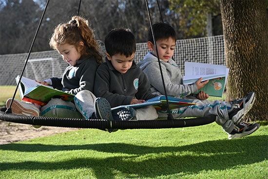 Children reading books on a swing in the park Three children sitting on a swing seat reading books in a sunny outdoor setting