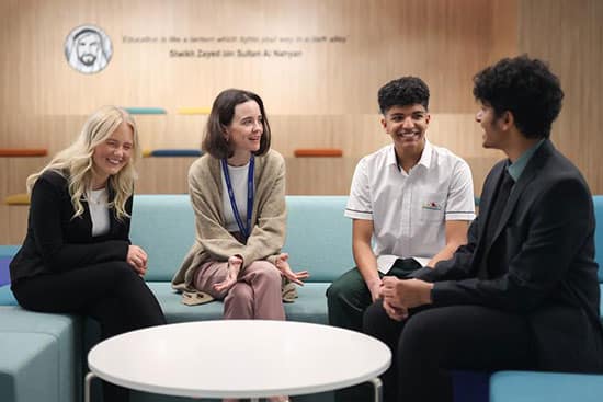 Collaborative group discussion in a contemporary setting with Arabic-inspired design Group of four people engaged in conversation in a modern setting with a background sign featuring Arabic text and a portrait