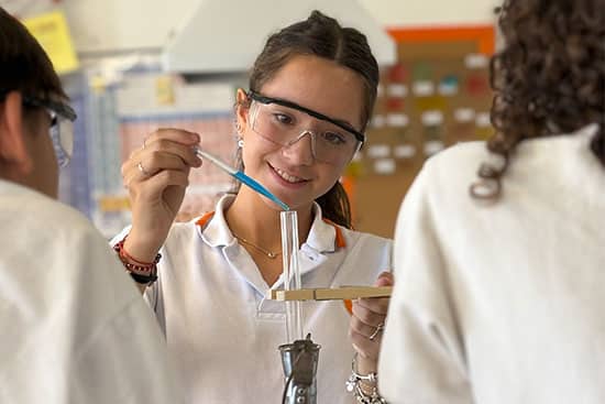 Student conducting an experiment in a laboratory A student in a lab coat performing an experiment in a science laboratory, using a pipette to add liquid to a test tube