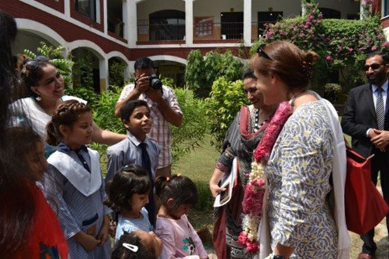 School children and teachers welcoming a guest with flowers during a community event.