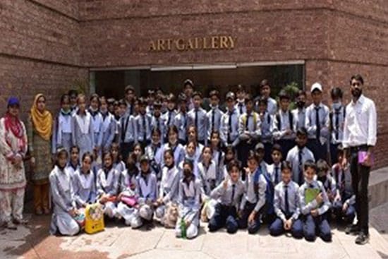 Group of school students and teachers posing for a photo outside an art gallery during an educational trip.