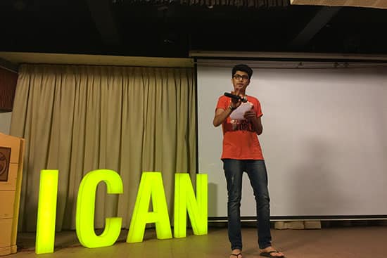 Student speaking on stage beside large illuminated I CAN letters during a school event.