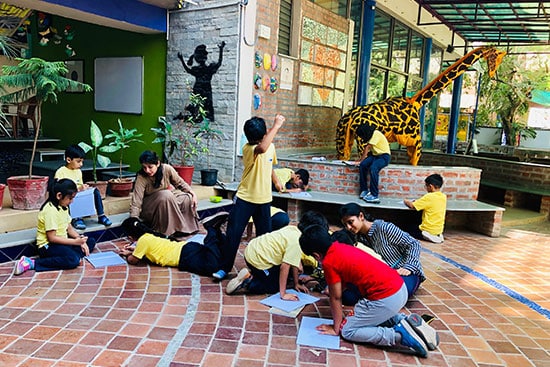 Young students engaged in outdoor learning activities with teachers in a creative school courtyard.