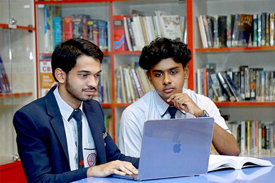 Students collaborating on a laptop in a library setting Two students working together on a laptop in a library, with bookshelves in the background