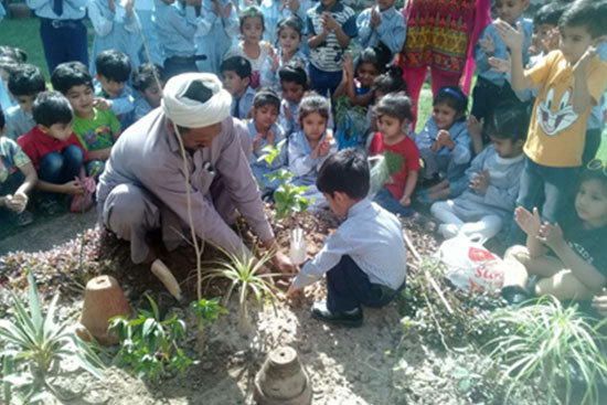 Young school children participating in a tree planting activity with guidance from a teacher.