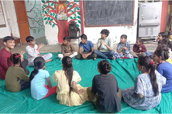 Group of children sitting in a circle on a mat, engaging in a group learning activity inside a classroom.