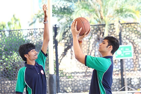 Two boys engaged in a friendly basketball game on a court Two boys playing basketball outdoors, one attempting to block a shot while the other is preparing to take a shot at the hoop