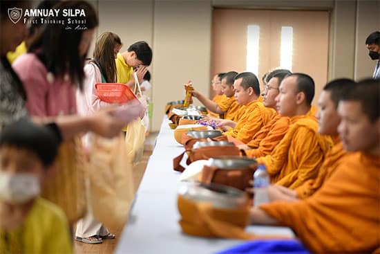 Students and teachers participate in alms-giving ceremony with Buddhist monks School community offering alms to Buddhist monks dressed in saffron robes during a religious ceremony.