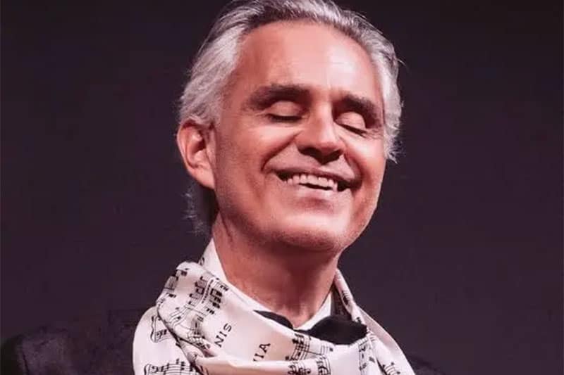 Andrea Bocelli smiling with eyes closed wearing a music note scarf