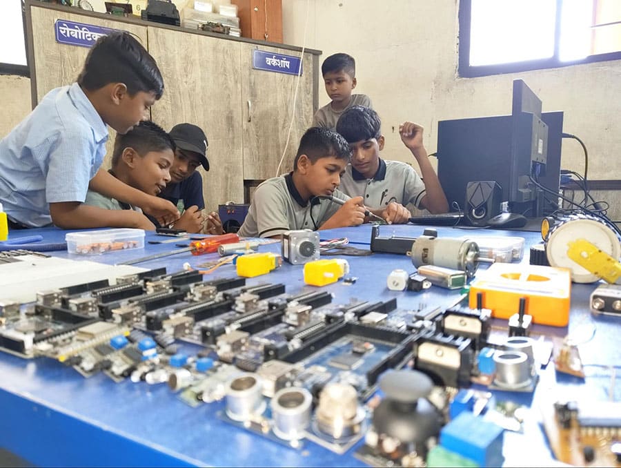 Group of students working with robotics parts and electronics in a classroom.
