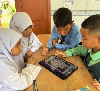Children sitting together at a school desk using a tablet for learning activities.