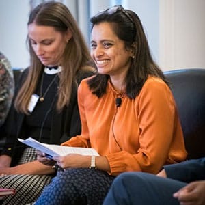 A woman in an orange blouse smiling while holding papers during a panel discussion.