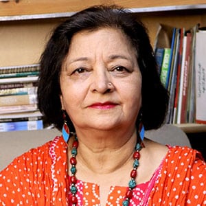 A woman in a red patterned outfit sitting in front of bookshelves, looking at the camera.