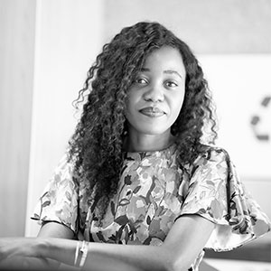 Black and white portrait of a woman with curly hair wearing a floral top, looking at the camera.