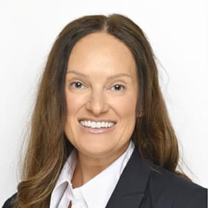 Smiling woman wearing a dark blazer and white shirt against a light background