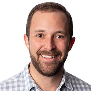 Smiling person with a short beard wearing a checkered shirt against a white background
