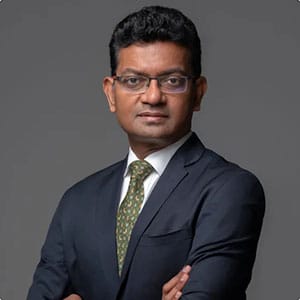 Person in a suit and glasses standing with arms crossed against a gray backdrop