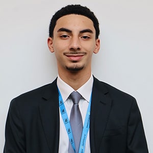 Smiling young man wearing a dark suit, tie, and lanyard