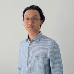 Portrait of a man wearing glasses and a light blue striped shirt standing against a plain background