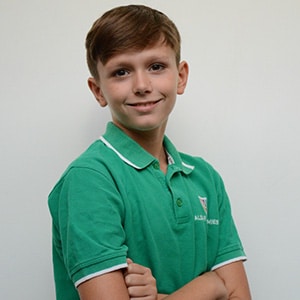 Smiling schoolboy in a green polo school uniform with arms crossed