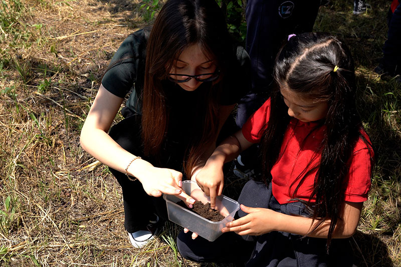 Student participating in a hands-on environmental science activity with guidance from an educator outdoors