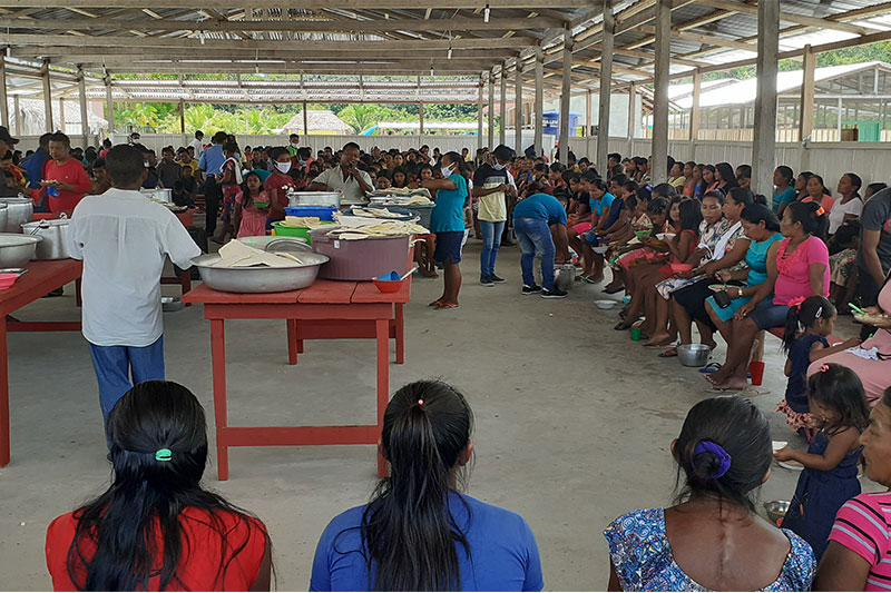 Community members participating in a large communal gathering and shared meal that promotes connection, culture, and collaboration.