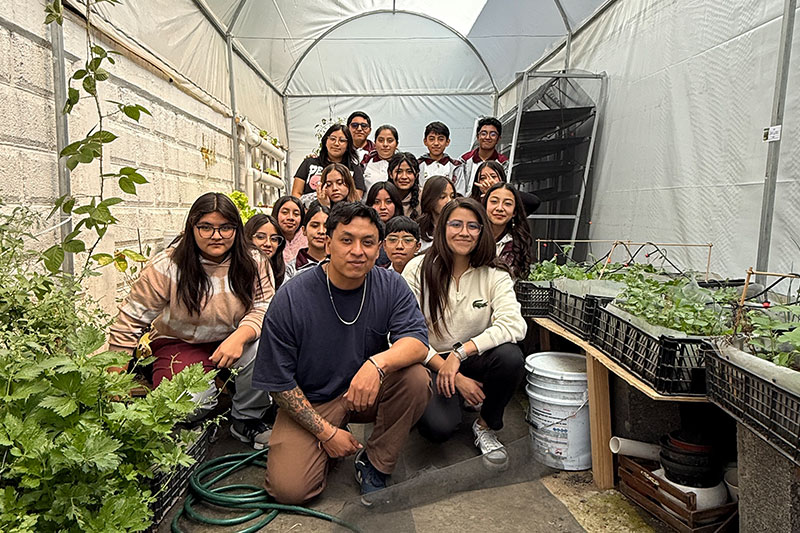 Students and an educator working together inside a greenhouse, learning about sustainable agriculture and plant cultivation.