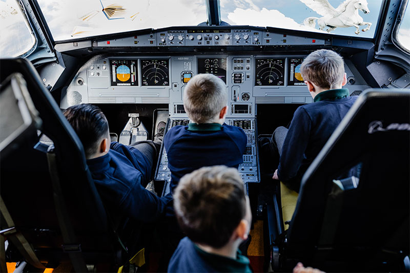 Students exploring an aircraft cockpit simulator during an immersive learning experience at Five Acre Wood School