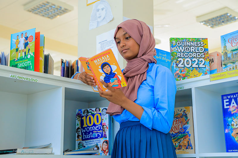 Student reading a book in a school library promoting literacy and lifelong learning through the Pharo Foundation