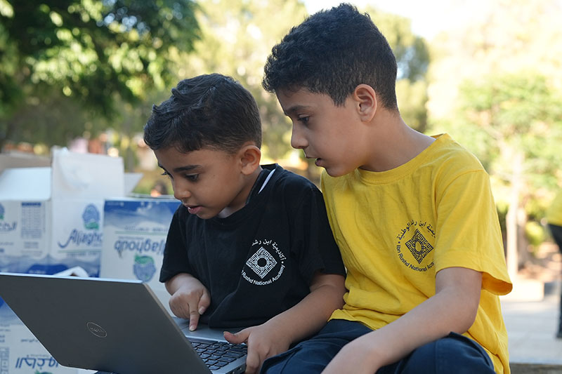 Two students using a laptop outdoors to develop digital literacy and technology skills at Ibn Rushd National Academy