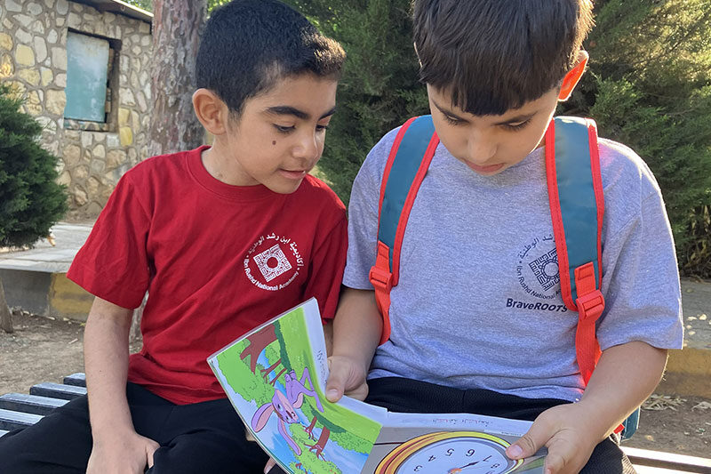 Two students reading a storybook together outdoors as part of literacy development at Ibn Rushd National Academy