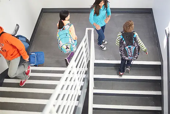Students carrying backpacks walking through a school stairwell with a teacher.
